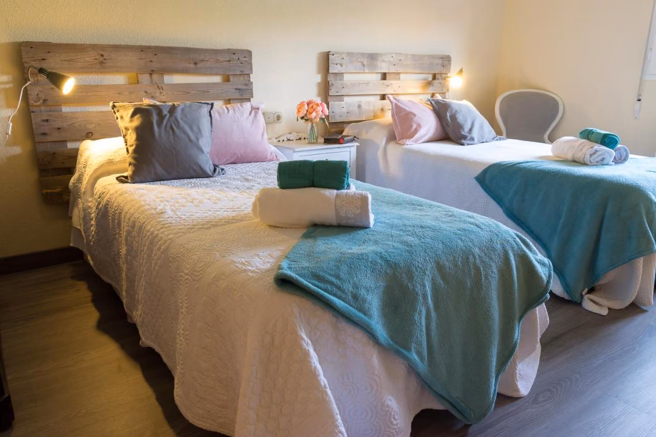Dormitorio con dos camas, cabeceros de palés de madera y lámparas de lectura