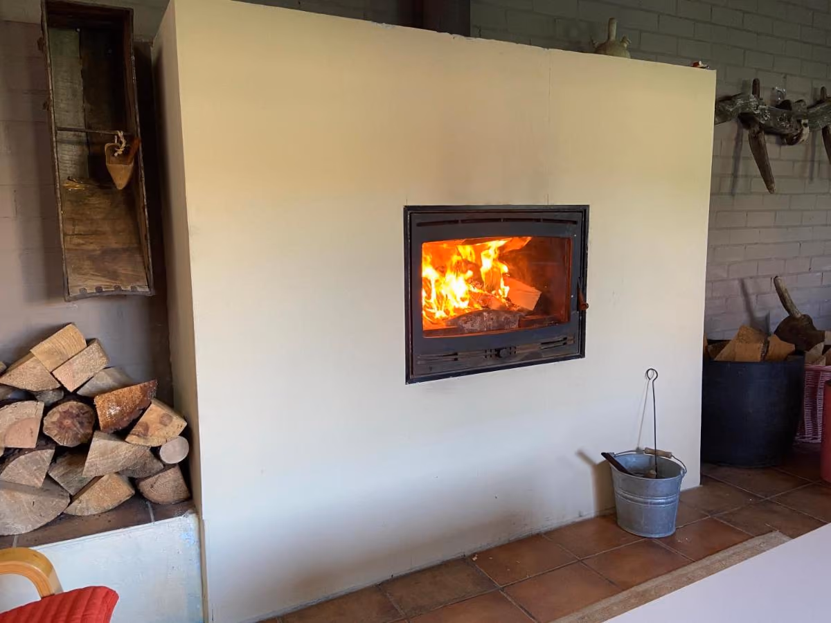 Chimenea del merendero encendida, con leña apilada al lado
